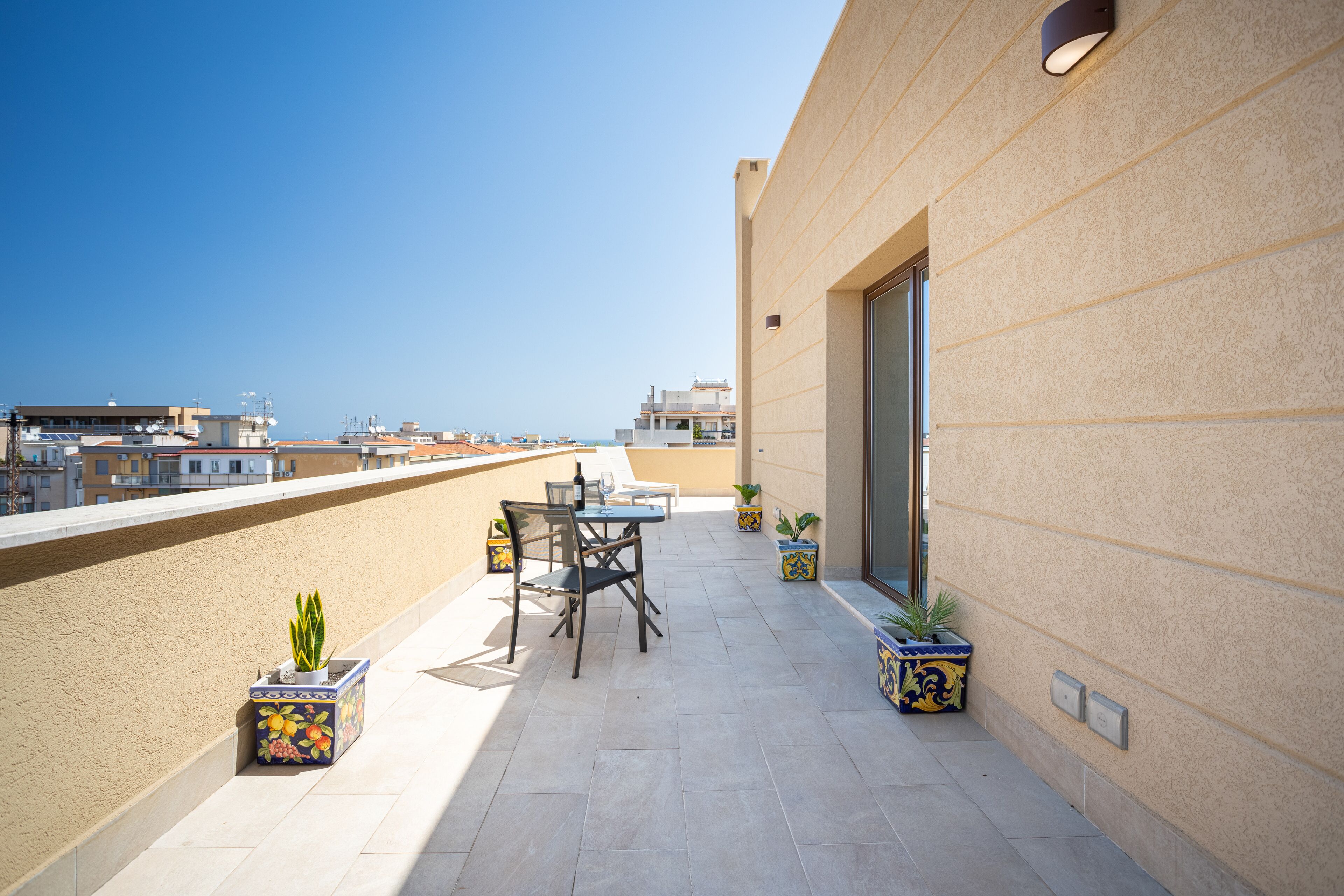 A rooftop terrace with a table and chairs, potted plants, and a view of the cityscape.