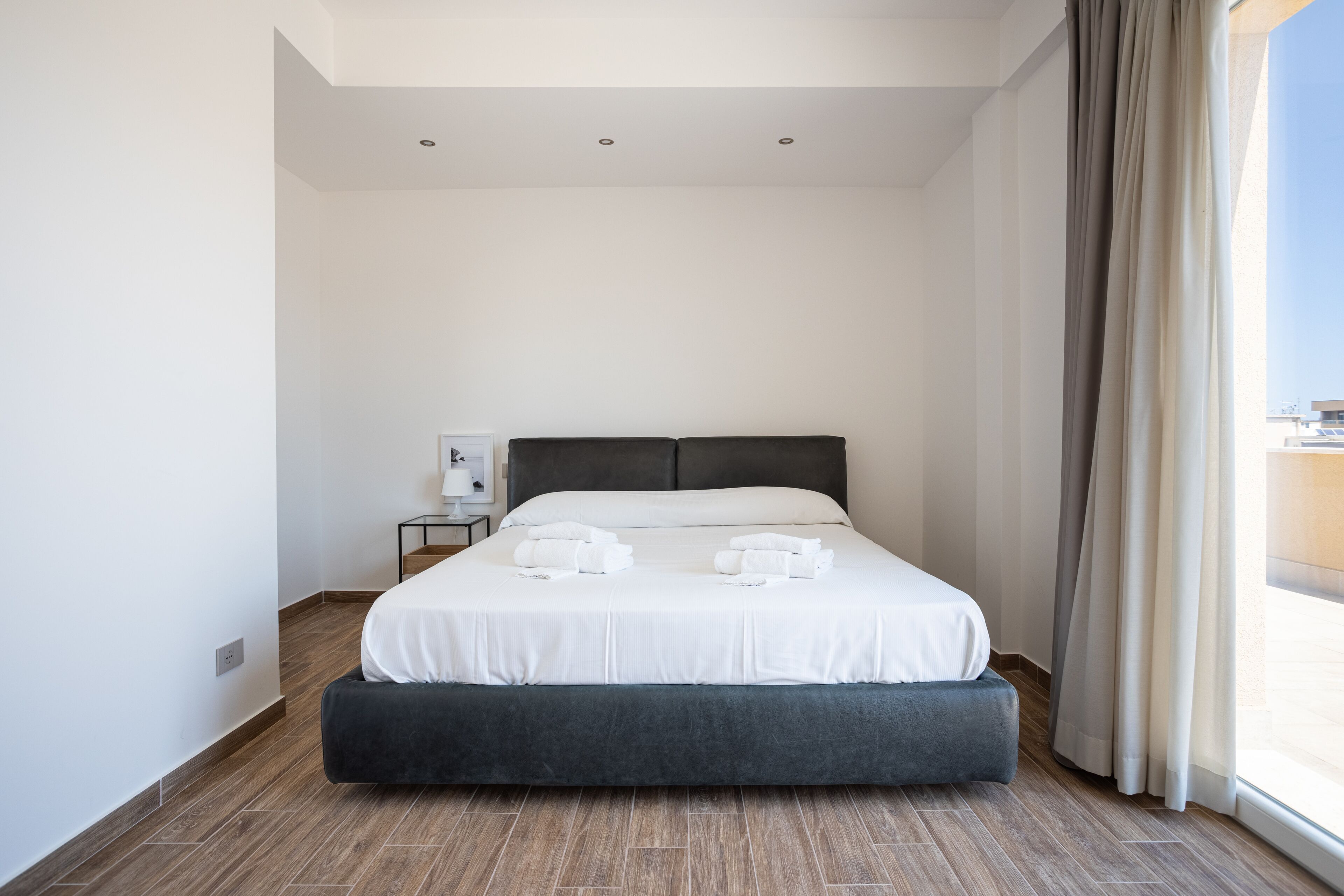 A modern hotel room with a large bed, a bedside table, and a view of the city.