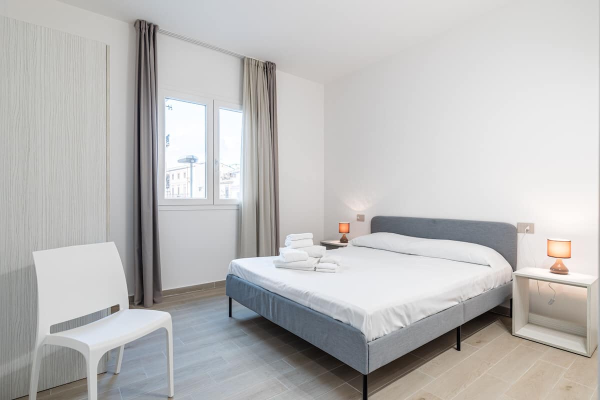A modern bedroom with a bed, a chair, a nightstand, and a window with curtains.