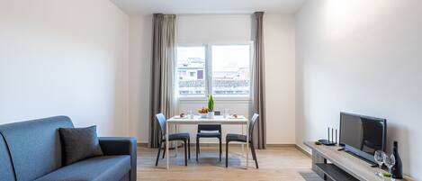 Una sala de estar moderna con sofá, mesa de comedor, sillas, televisor y ventana con cortinas.