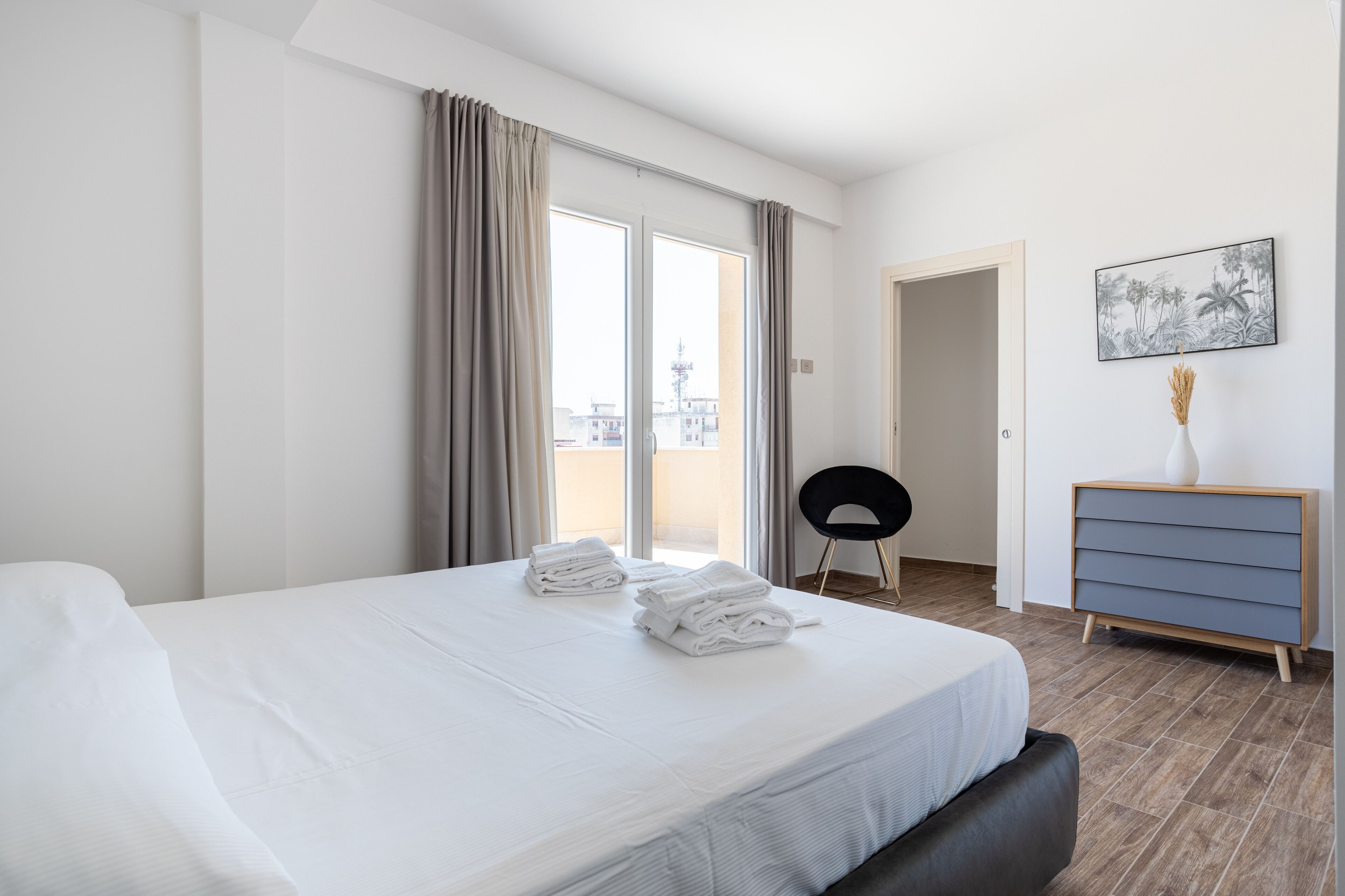 Ett modernt hotellrum med en stor säng, en byrå, en stol och utsikt över staden genom fönstret.