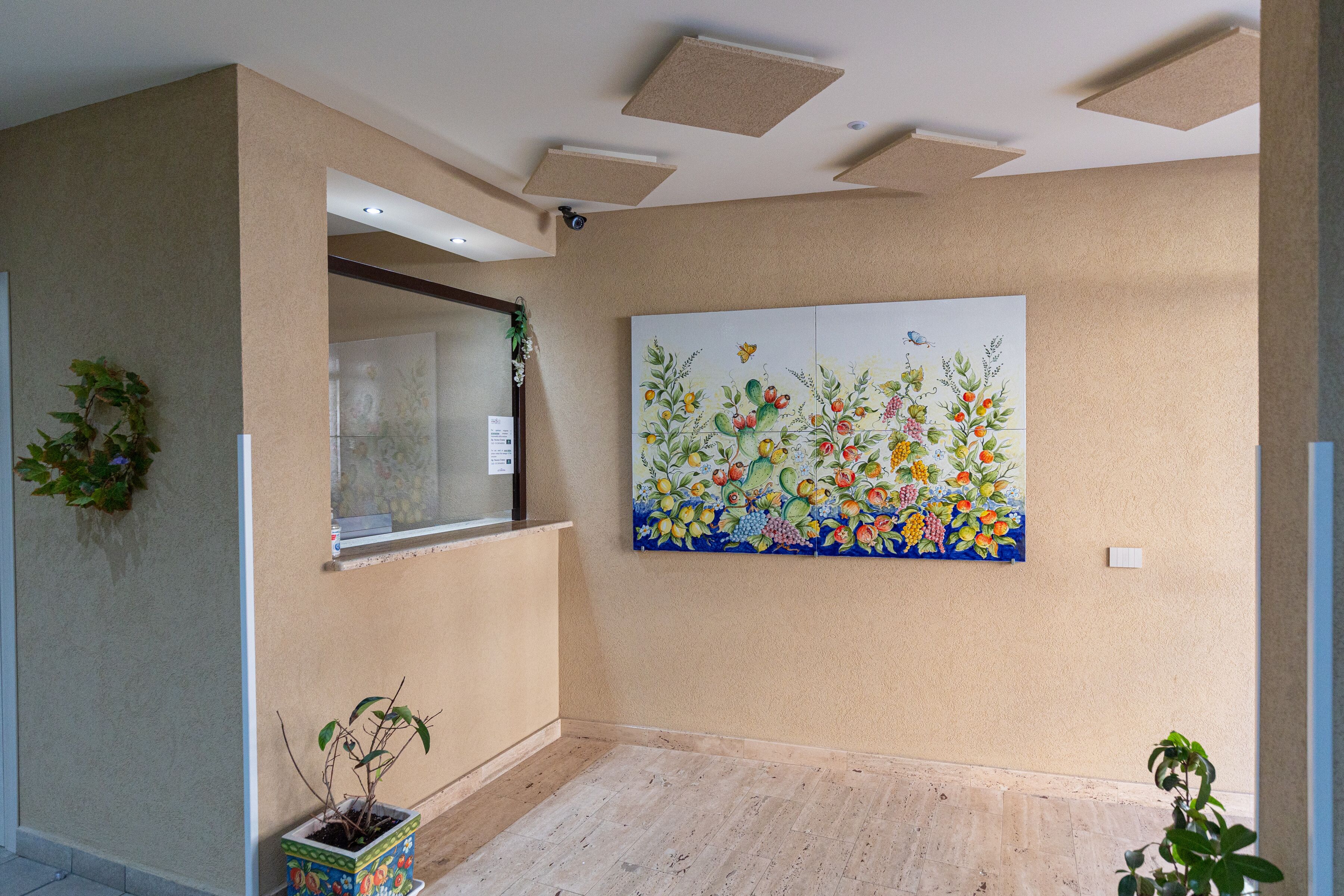 Una habitación con pared color beige, un cuadro floral grande, una ventana con vistas y una planta en maceta.