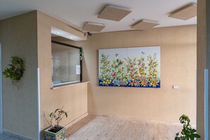 A room with a beige wall, a large floral painting, a window with a view, and a potted plant. - Multisuite Palermo (Palermo)