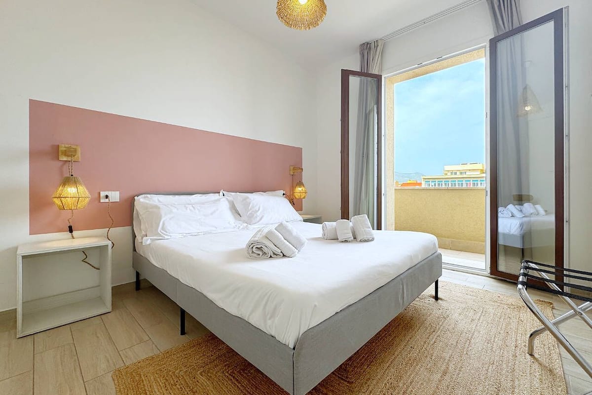 A modern bedroom with a bed, bedside tables, and a view of the outside.