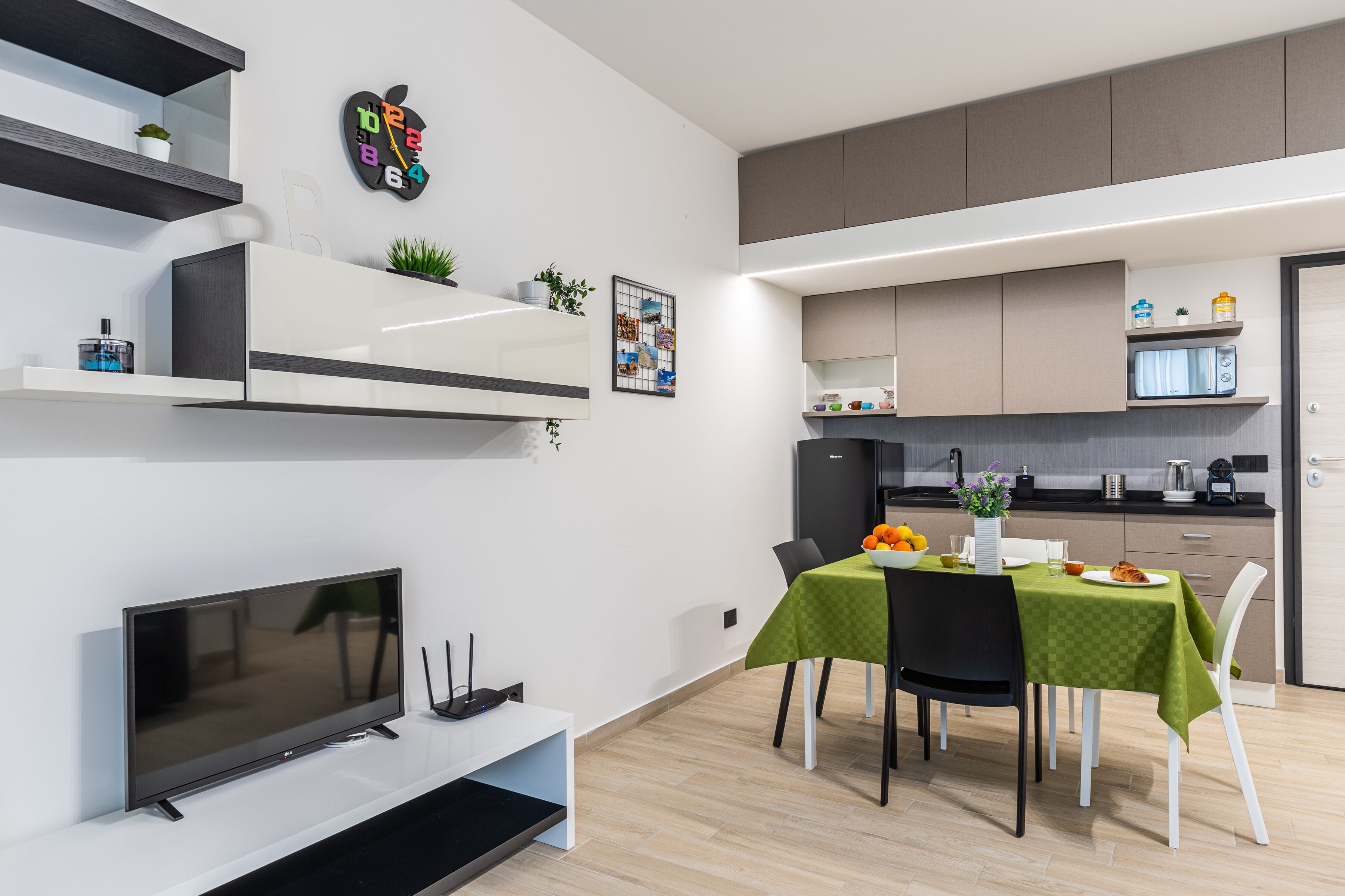 Eine moderne Küche mit integrierten Geräten, ein Essbereich mit grüner Tischdecke und ein Flachbildfernseher auf einem weißen Schrank.