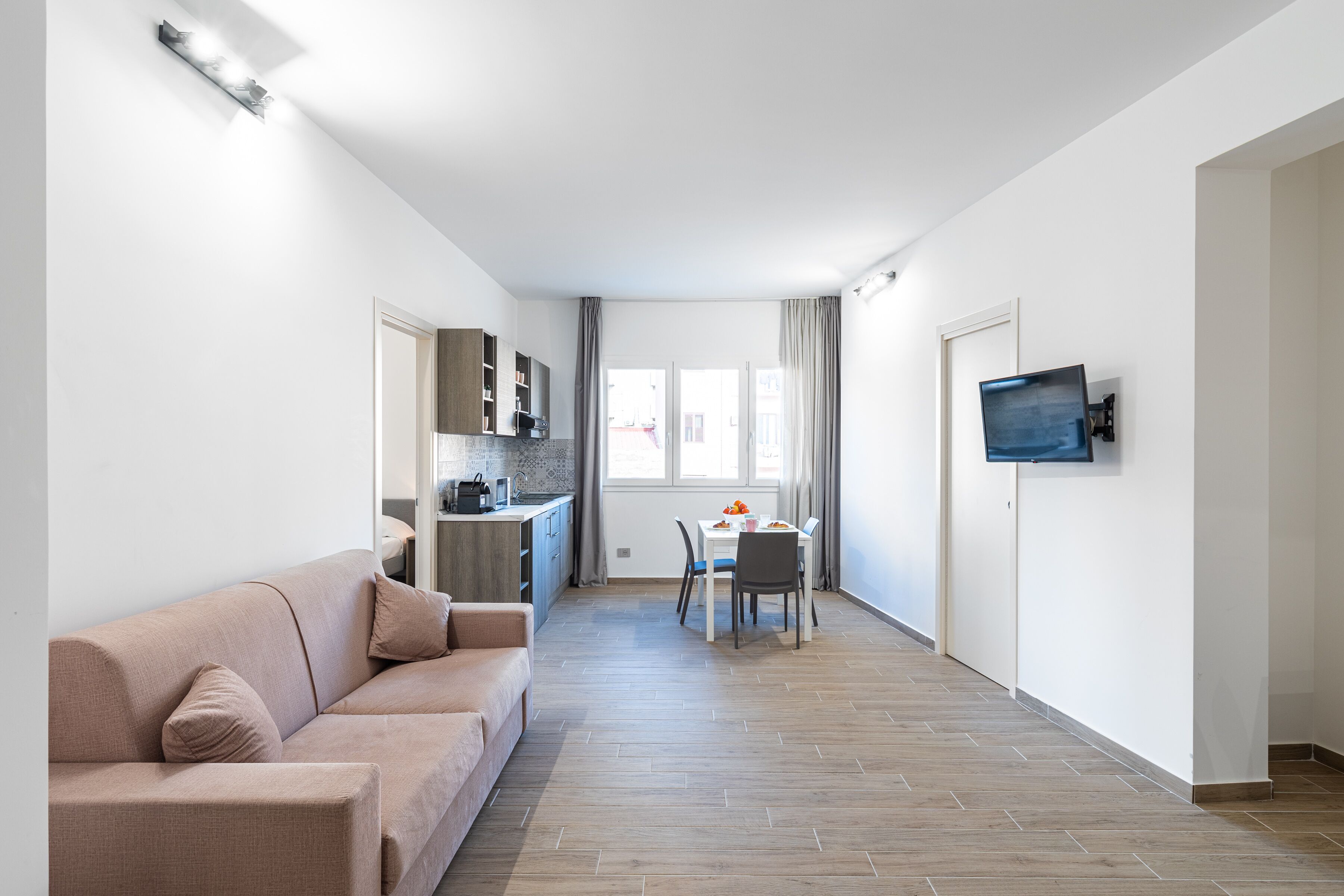 A modern apartment with a living room, kitchenette, dining area, and a TV mounted on the wall.