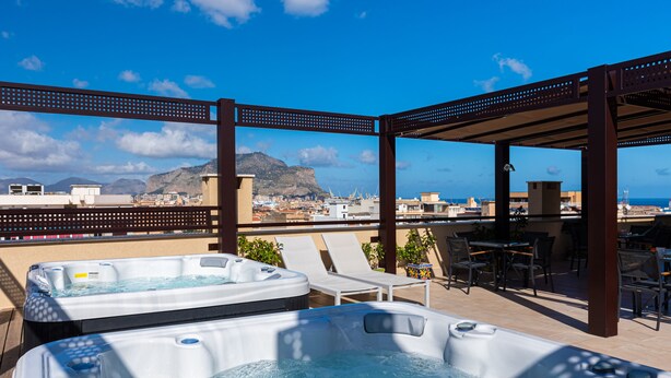 A rooftop terrace with two hot tubs, lounge chairs, and a covered dining area overlooking a cityscape and mountains. - Multisuite Palermo (Palermo)