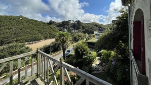 A balcony with a view of a hillside, a road, and a building with a red door. - Seaside villa next to the GR34  (Ploumilliau)