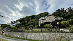 A stone house with a balcony, surrounded by lush greenery and a stone wall. - Seaside villa next to the GR34  (Ploumilliau)
