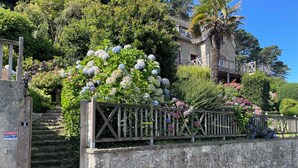 A stone wall with a wooden fence, a staircase leading to a house, and a variety of flowering plants. - Seaside villa next to the GR34  (Ploumilliau)