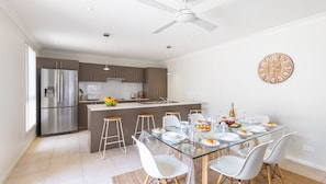 A modern kitchen with a central island, stainless steel appliances, and a dining area with a glass table and white chairs.