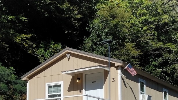 Ein Bungalow-ähnliches Mobilheim mit Veranda, einer amerikanischen Flagge und einer kleinen angebauten Garage.