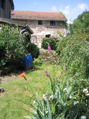 A stone building with a tiled roof, surrounded by a garden with various plants and flowers. - Charming stone house restored in English style (Arfeuilles)