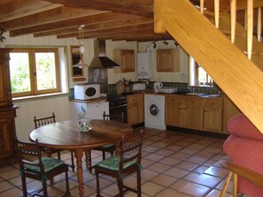 A kitchen with wooden cabinets, a dining table with chairs, a washing machine, and a staircase. - Charming stone house restored in English style (Arfeuilles)