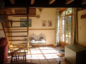 A room with a wooden ladder, a bed with a metal frame, a small table, and a window with curtains. - Charming stone house restored in English style (Arfeuilles)