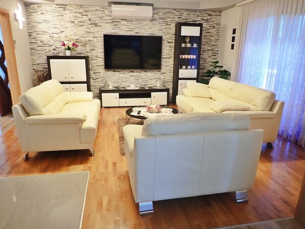 A modern living room with two white sofas, a flat-screen TV, a decorative shelf, and a wooden floor.