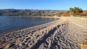 En strand med fodspor i sandet, en klar himmel og bjerge i baggrunden.
