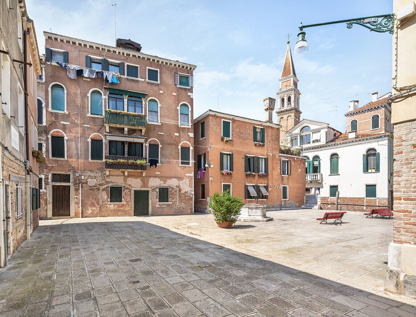 A narrow street with historic buildings, a church tower, and a small plaza with benches.