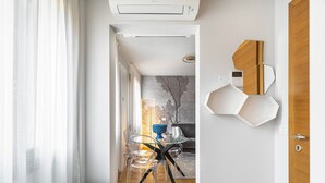Un corridoio moderno e ben illuminato con vista diretta su una sala da pranzo, caratterizzato da un pavimento in legno, un tavolo in vetro e una panca blu.