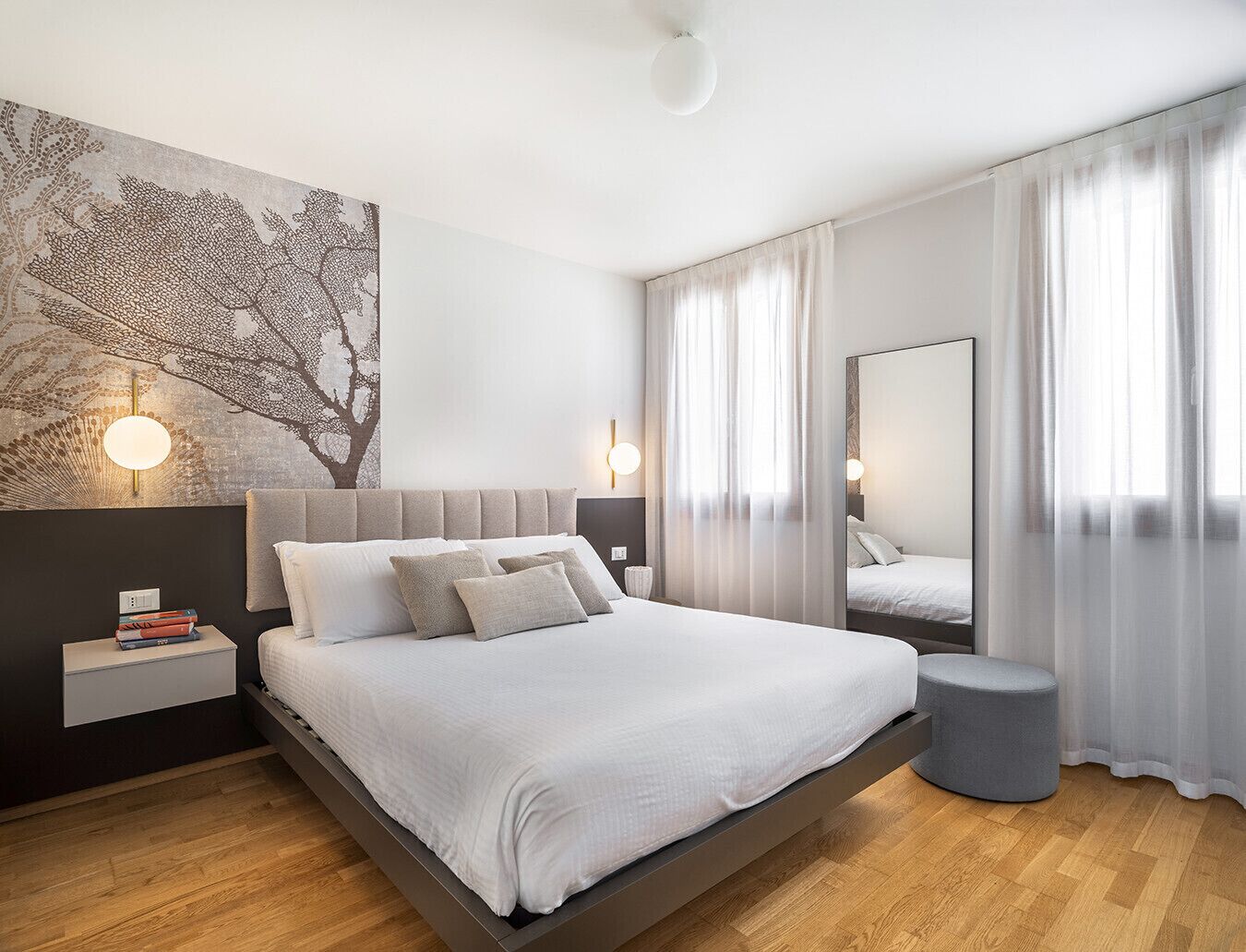 Un dormitorio moderno con una cama grande, mesitas de noche, una lámpara de pared y un espejo.
