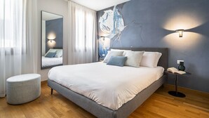 Ein modernes Schlafzimmer mit einem großen Bett, einem runden Hocker, einem Spiegel und einer Wandleuchte.