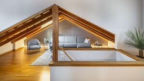 Ein modernes Schlafzimmer im Loft-Stil mit schrägem Dach, Holzbalken, einem grauen Sofa und einem kleinen Tisch mit einer Pflanze.