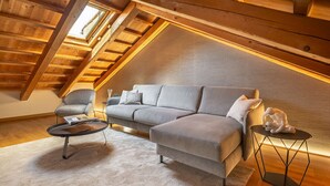 Ein gemütliches Schlafzimmer im Loft-Stil mit schrägem Dach, einem grauen Sofa, einem kleinen runden Tisch und einem Stuhl.