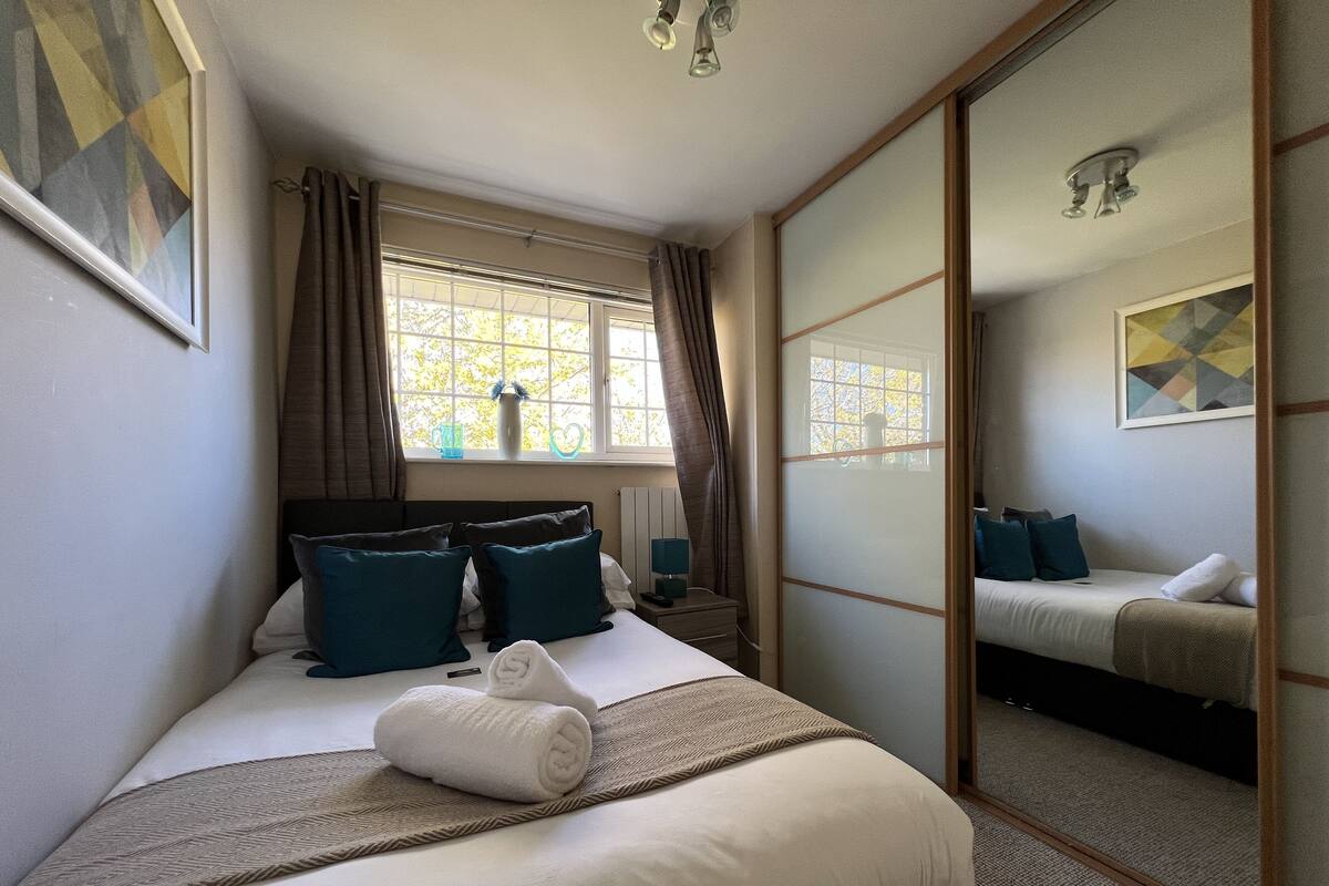 Una habitación de hotel con una cama grande, una mesita de noche, un espejo y una ventana con cortinas.