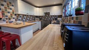 A modern kitchen with white cabinets, a wooden island, red stools, and a black toaster. - Lancaster Close Serviced Accommodation (Bicester)