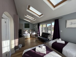 Un dormitorio moderno con dos camas, un sofá, un televisor y un amplio ventanal con luz natural.
