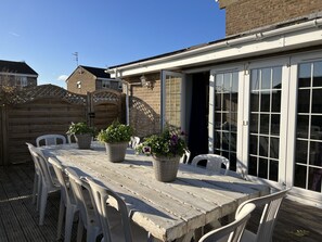 A wooden deck with a table and chairs, potted plants, and a brick wall. - Lancaster Close Serviced Accommodation (Bicester)