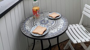A balcony with a table set for two, a bottle of juice, and a plate of toast. The view includes a sandy landscape and a cloudy sky.