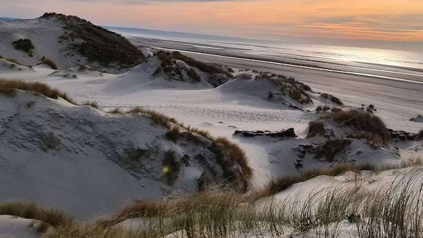 A beach landscape with sand dunes and a sunset.