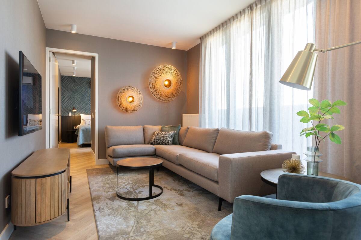 A modern living room with a sofa, armchairs, a coffee table, and a TV.