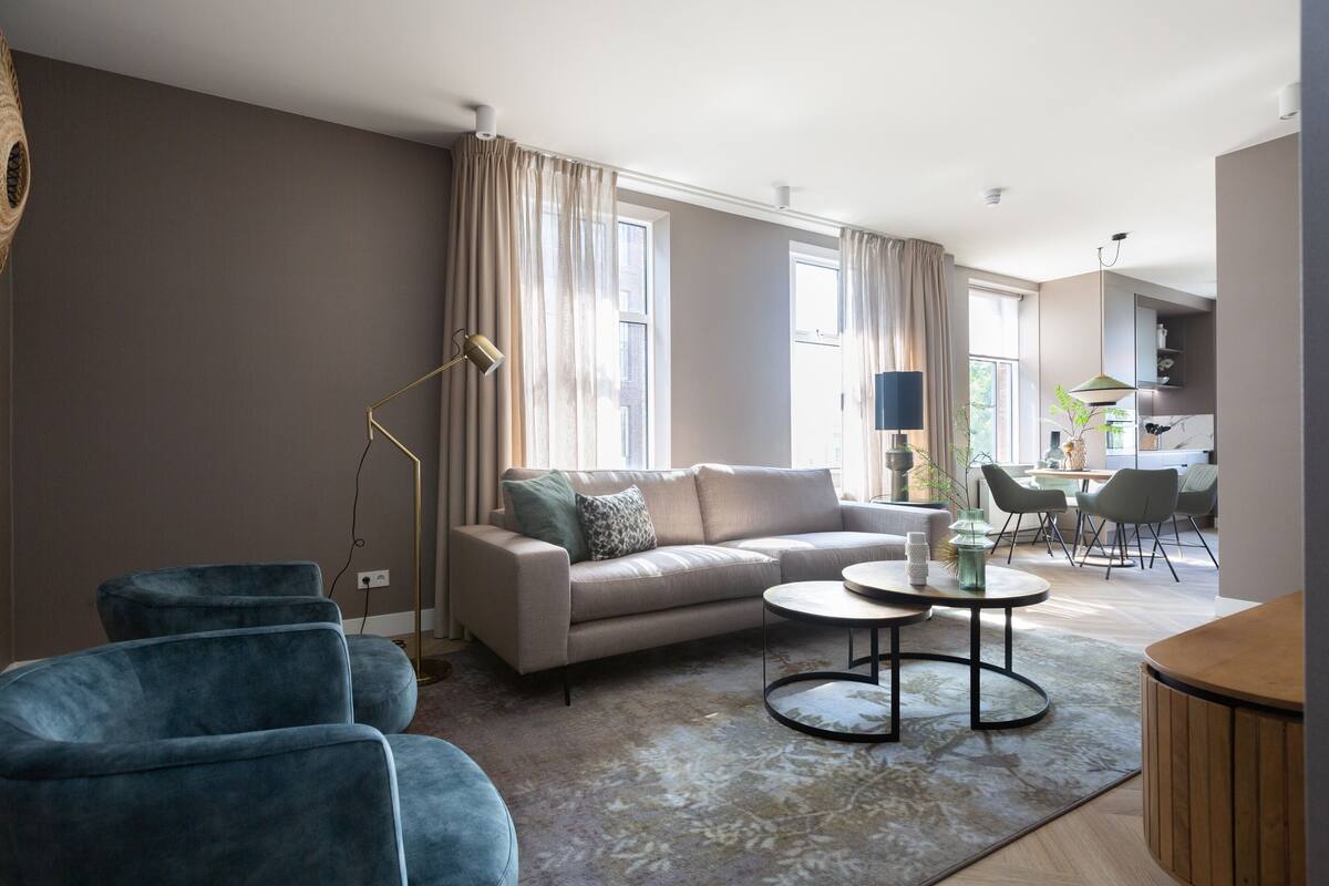 A modern living room with a sofa, two armchairs, a coffee table, and a dining area with chairs.