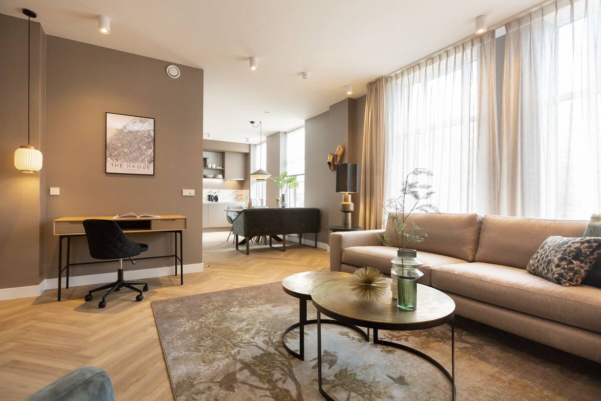 A modern living room with a sofa, coffee table, and office chair. There is a dining table with chairs in the background.