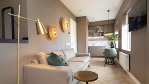 Una sala moderna con un sofá, una mesa redonda de centro y una lámpara de pie. Se ve un área de cocina al fondo con una mesa de comedor y sillas.
