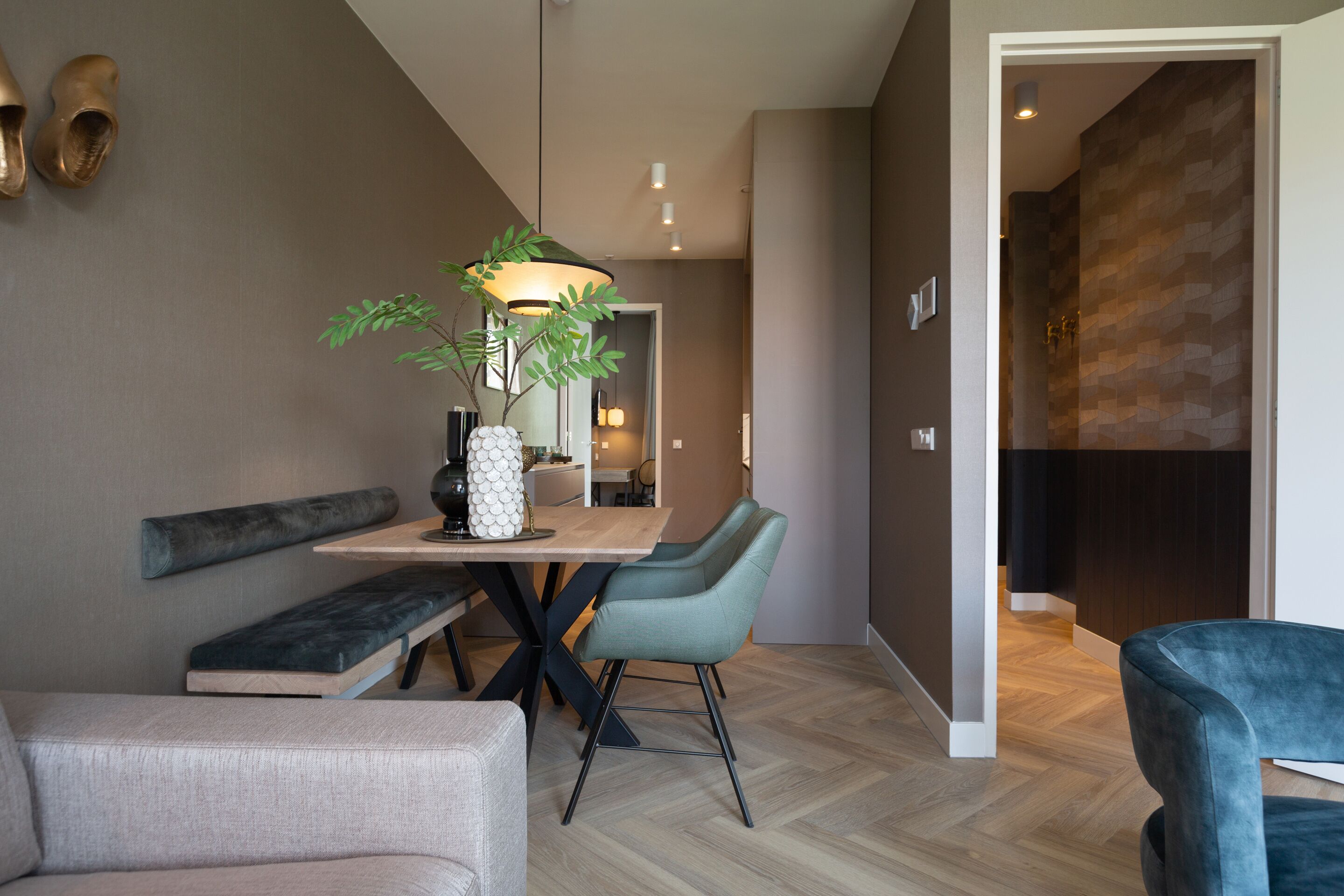 Een moderne eetruimte met een houten tafel, twee stoelen, een bankje en een plant in pot.
