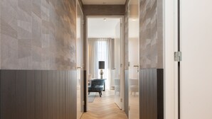 Un pasillo con suelo y paredes de madera que conduce a una habitación con una silla azul y una lámpara.