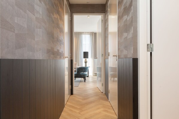 Un pasillo con suelo y paredes de madera que conduce a una habitación con una silla azul y una lámpara.