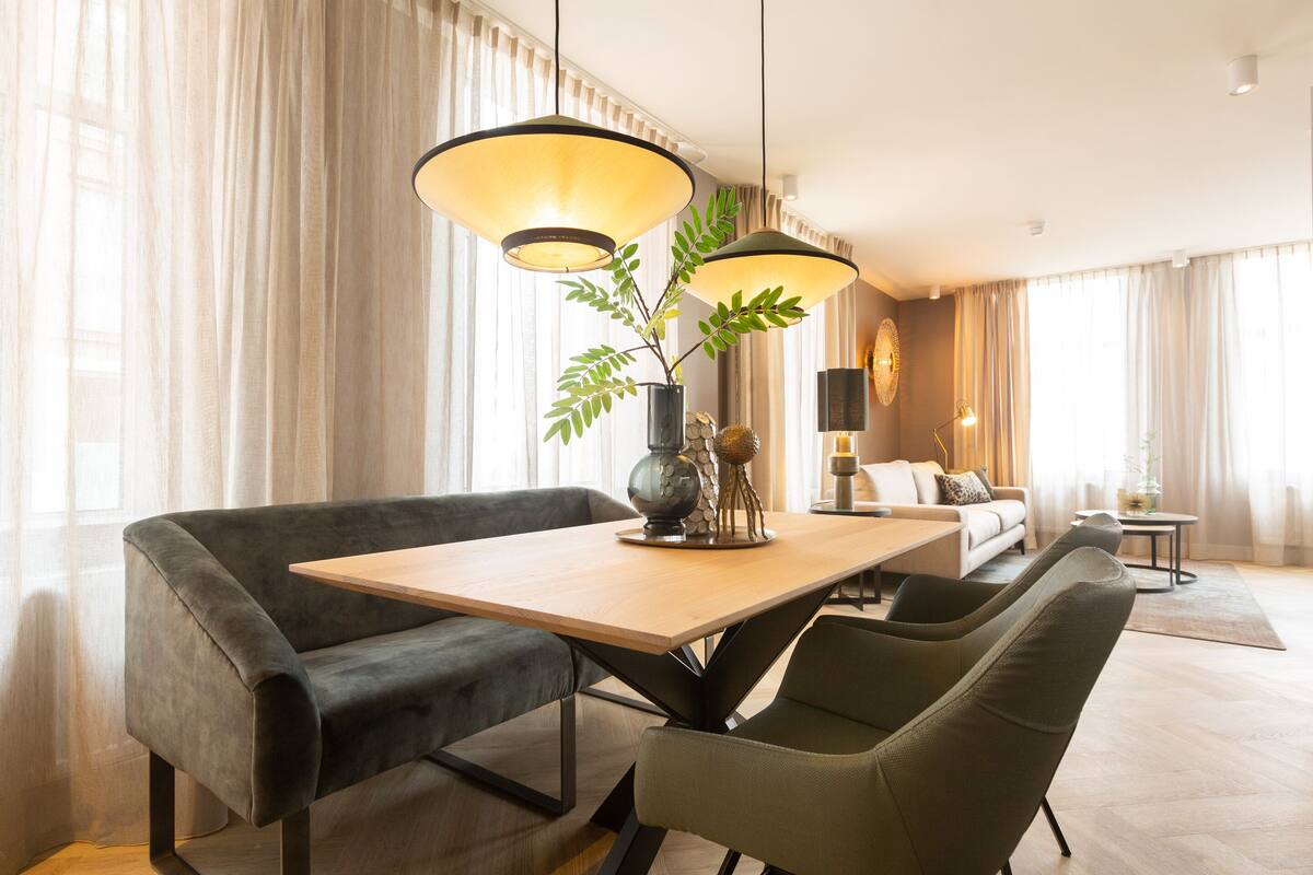 A modern living room with a dining area, featuring a sofa, chairs, a table, and a large window with curtains.