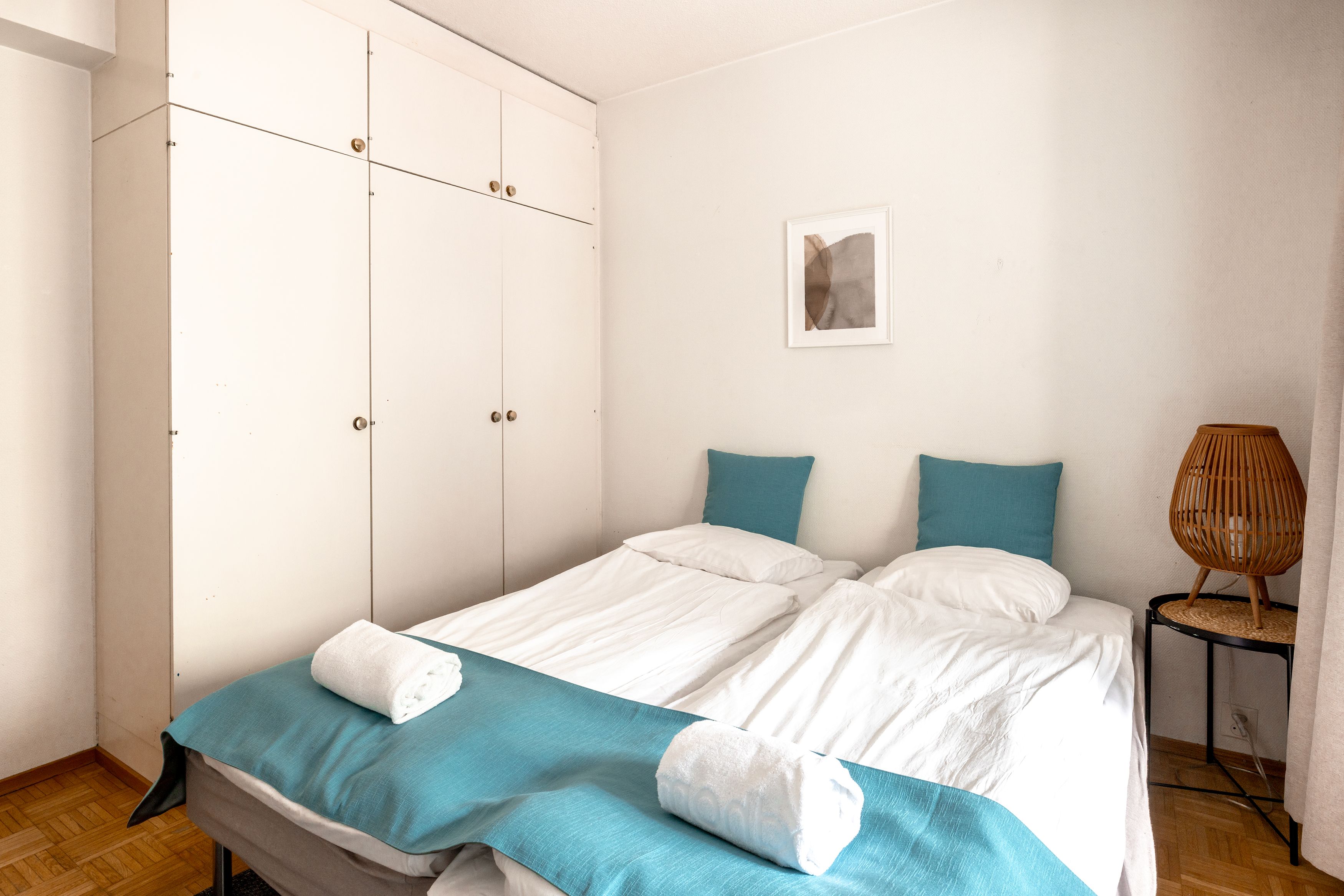 Un dormitorio con una cama, un armario, una lámpara de noche y una obra de arte colgada en la pared.