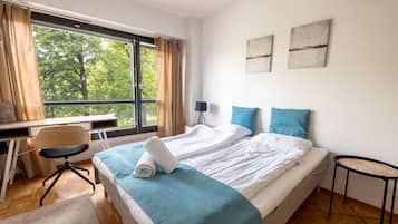 A hotel room with a bed, a desk, a chair, and a view of trees through the window.
