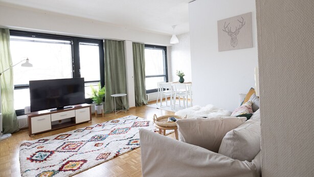 A living room with a sofa, a TV, a dining table with chairs, and a patterned rug. - Cozy 95m2 home With Sauna In Kaisaniemi (Helsinki)