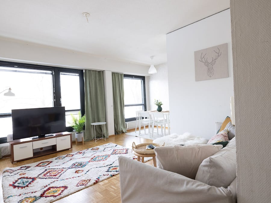Ein Wohnzimmer mit einer Couch, einem Fernseher, einem Esstisch mit Stühlen und einem gemusterten Teppich.