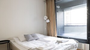 A bedroom with a bed, a bedside table, a lamp, and a window with curtains. - Cozy 95m2 home With Sauna In Kaisaniemi (Helsinki)