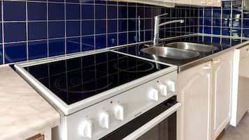 A kitchen with a black stovetop, a stainless steel sink, and white cabinets.