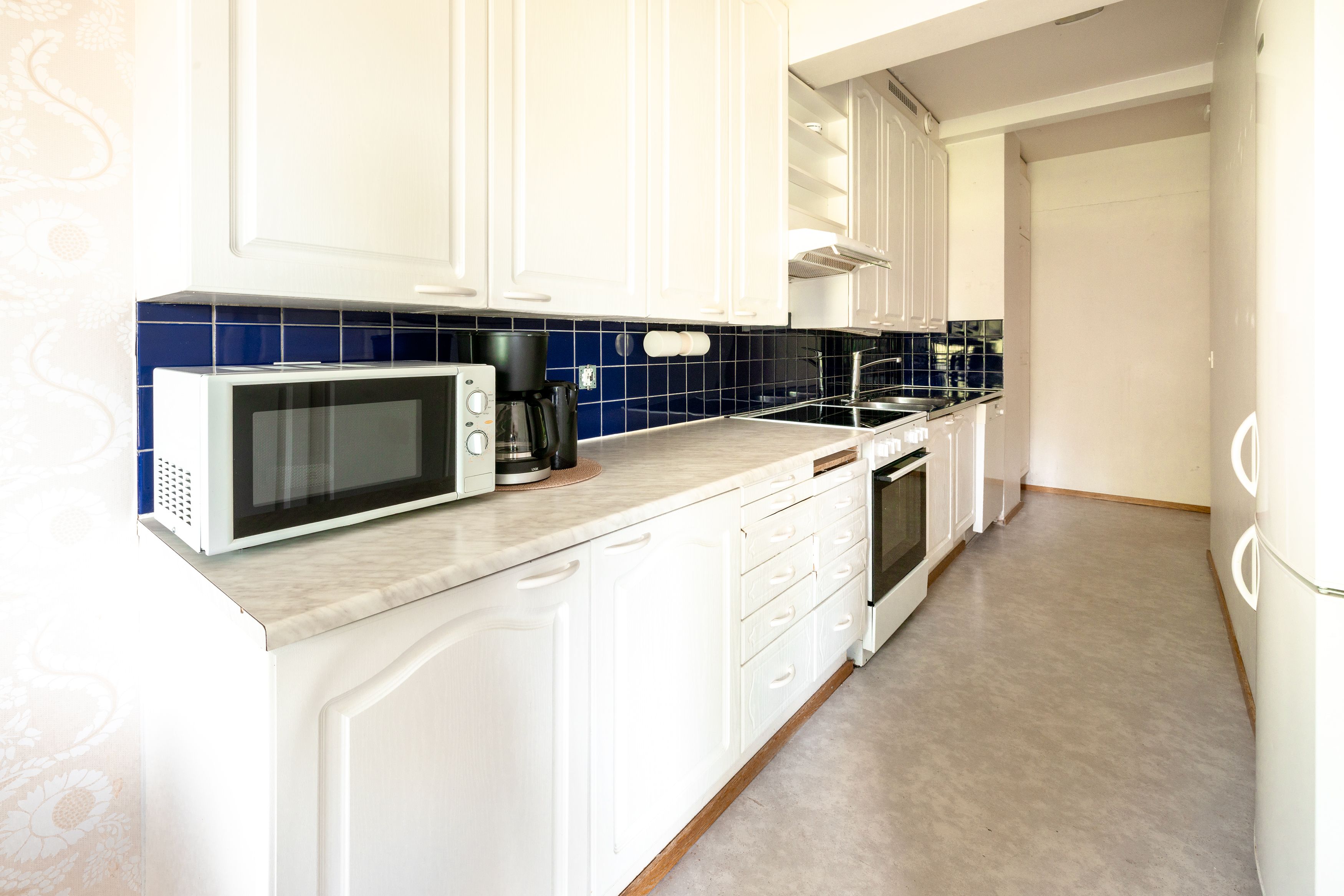 A kitchen with white cabinets, a microwave, a coffee maker, and a sink.