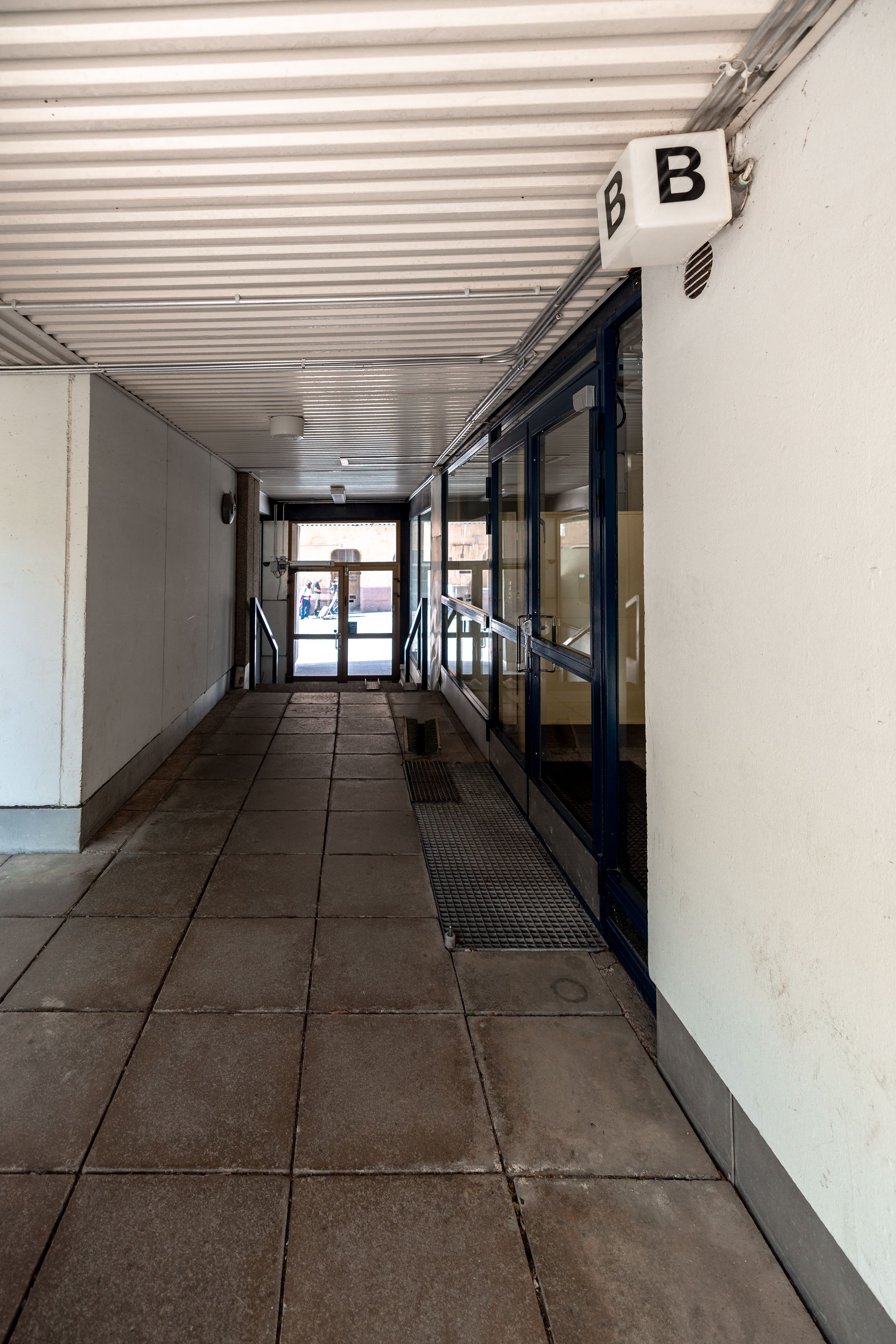 A corridor with a tiled floor, metal railings, and a door leading outside.