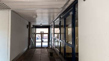 A corridor with a tiled floor, metal railings, and a door leading outside.